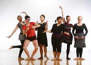 A group of adult dancers in various casual outfits make a silly pose for the camera