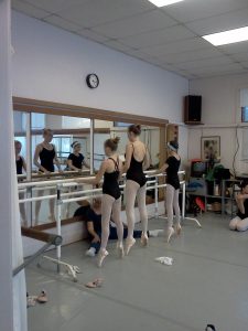 Three dancers in pointe shoes practice at the barre
