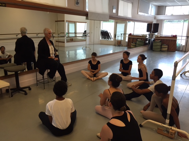 A group of students sit around Beth Hoge during class instruction