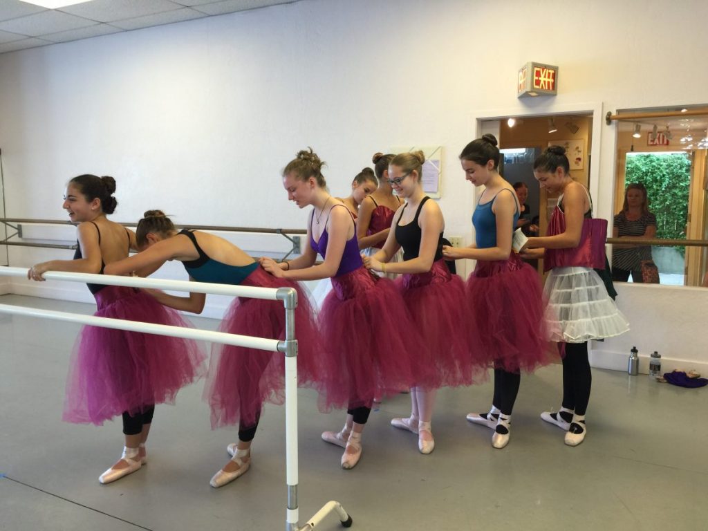 Dancers try on costumes and help each other fasten their tutus