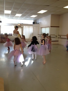 Young dancers at a Ballerina Birthday Party wear purple skirts and dance with a teen dancer in costume