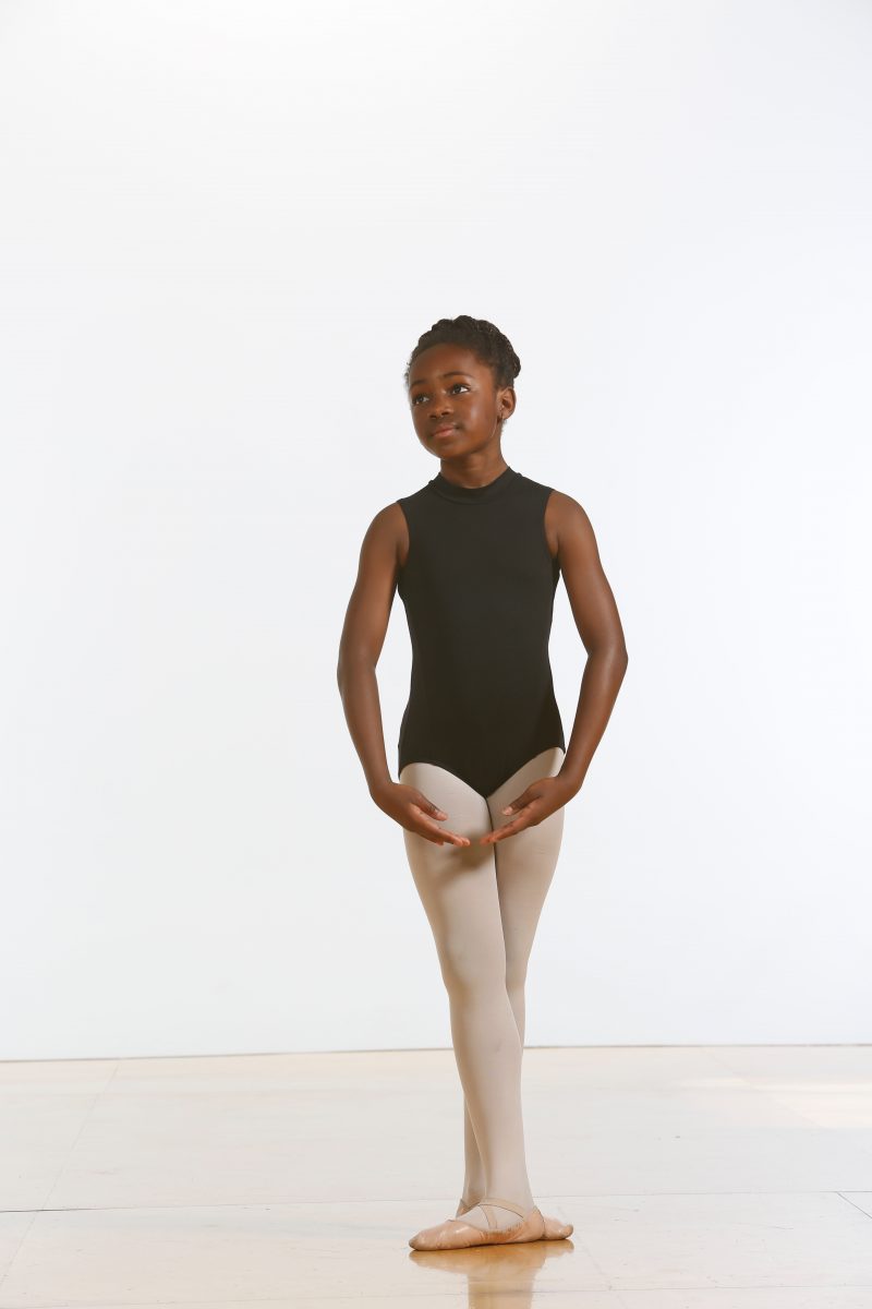 One dancer in a black leotard and pink tights stands in 5th position.