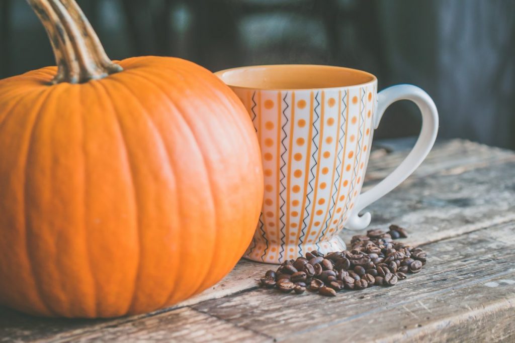 Stock photo of a pumpkin next to a mug with coffee beans on the table in front.