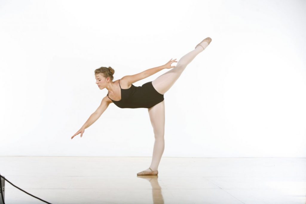 A dancer in a black leotard and pink tights en penche.