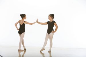 Two young dancers in tendu touching the palms of one hand together