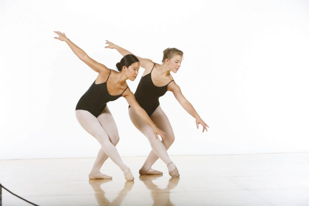 Two dancers in black leotards and pink tights pose