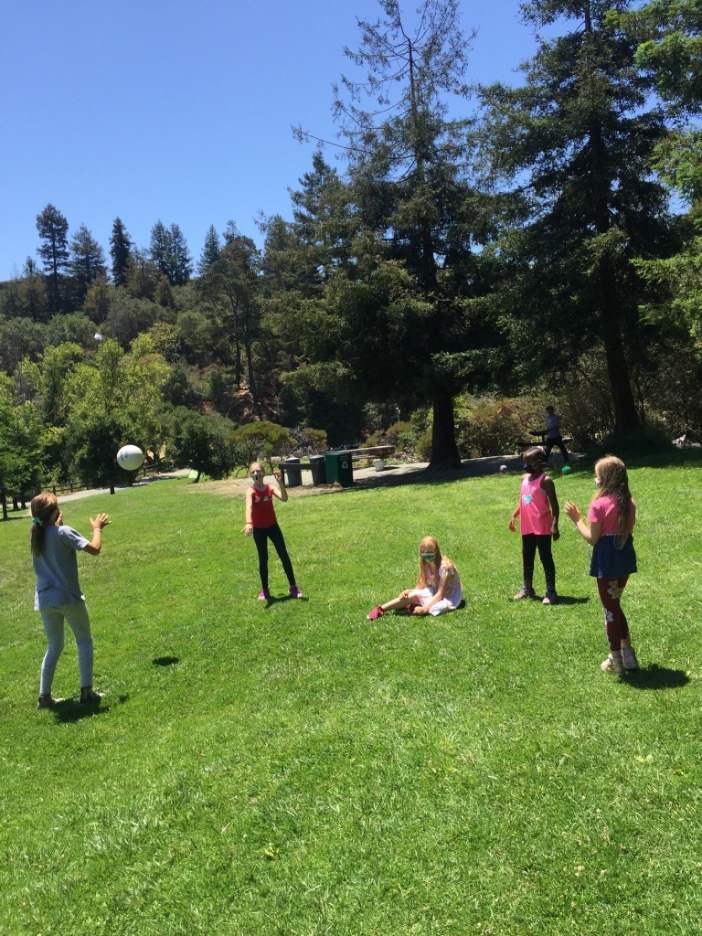 Dancers taking a break during summer dance camp at a park, playing with a ball.