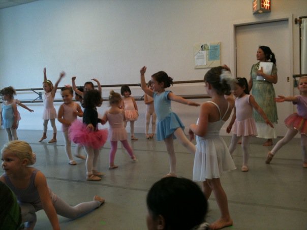 A group of young dancers practicing for an in-studio performance with their teacher standing off to the side.